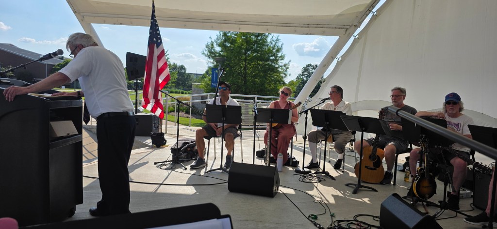 Photo of Prof. Michael Harkness discussing the Declaration of Independence at Harper College, July 8, 2026 with members of the Back Porch Revue seated on stage.